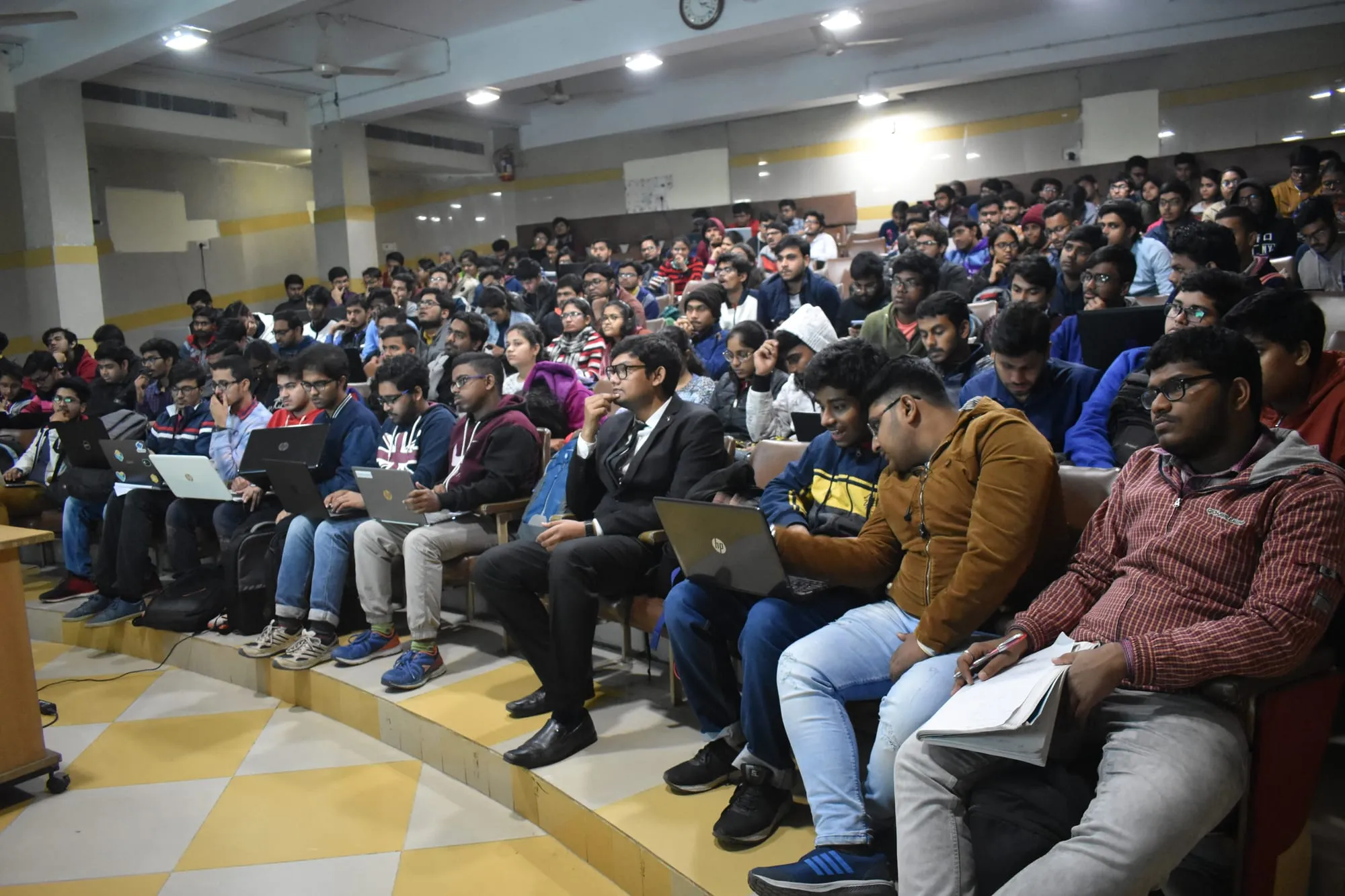 A lecture hall full of students, many with laptops open.