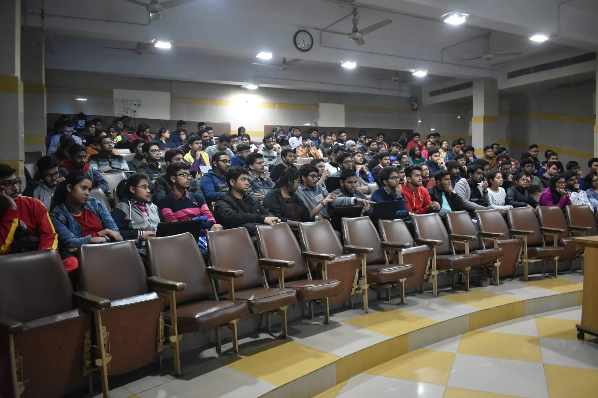 A full lecture hall seen from the side, every row taken.